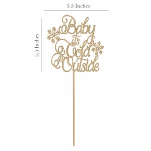 May include: Gold glitter cake topper with the text "Baby It's Cold Outside" and snowflake accents. The topper is 5.5 inches tall.