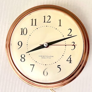 May include: A round, vintage Westclox electric clock with a copper-colored bezel. The clock face is cream-colored with black numerals and hands. The clock reads 8:12. The text "WESTCLOX electric" is printed at the bottom of the clock face.