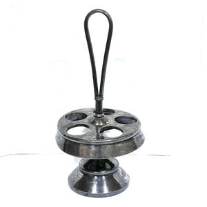 May include: A silver-toned metal egg holder with a circular base and six egg-shaped openings. It features a handle that arches upwards. The holder has a tiered design, with a wider base and a narrower top section.