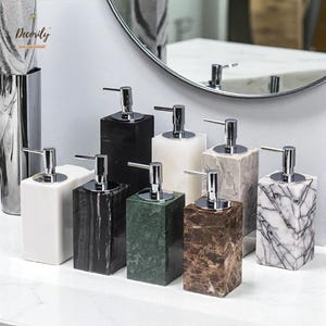 May include: A selection of rectangular soap dispensers in various colours and patterns, including white, black, green, and marble. Each dispenser has a silver pump and a square base, ideal for bathroom decor.