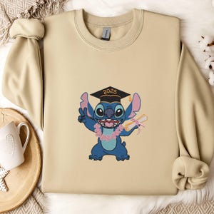 May include: Beige sweatshirt featuring a blue cartoon character wearing a graduation cap with "2025" on it. The character is holding a diploma and a pink flower lei, making a peace sign. The sweatshirt has long sleeves.