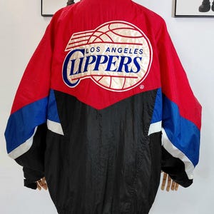 May include: A red, black, and blue Los Angeles Clippers Starter jacket. The jacket features the team's logo on the back and a Starter logo on the collar. The jacket is displayed on a mannequin.