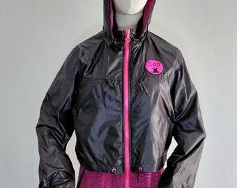 Könnte beinhalten: Schwarze Kapuzenjacke mit pinkfarbenem Reißverschluss und einem pink-schwarz gestreiften unteren Teil. Die Jacke hat einen pinkfarbenen Aufnäher mit dem Wort "Cop" und einer Stern-Grafik. Die Jacke wird auf einer Schaufensterpuppe präsentiert.