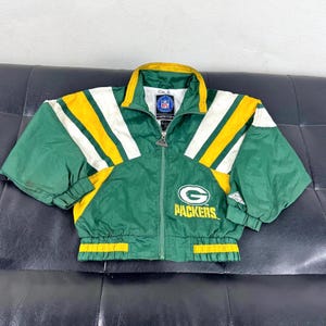 Può includere: Giacca verde e gialla dei Packers con dettagli bianchi. La giacca presenta una cerniera completa, un colletto rialzato e il logo dei Packers sul petto. La giacca è realizzata in materiale leggero.