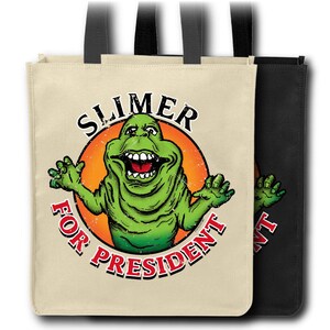 May include: Two tote bags, one beige and one black, with black handles. The beige bag features a green cartoon character with the text "SLIMER FOR PRESIDENT" in a circular design. The black bag has a partial view of the same design.