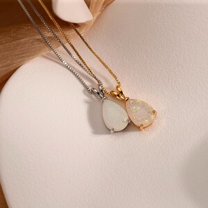 May include: Two necklaces with teardrop-shaped opal pendants. One pendant is set in silver, the other in gold. The opals display a play of color, with flashes of white, yellow, and orange. The chains are delicate.