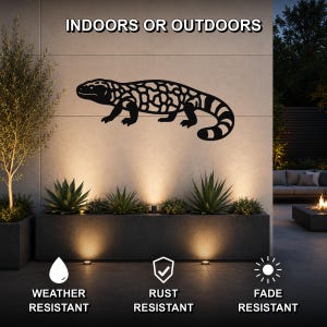 Black metal Gila monster wall art with intricate cutout patterns, mounted on an outdoor wall above a planter in a modern patio setting.