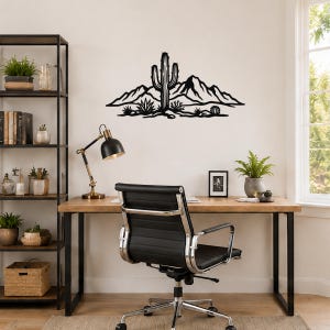 Black metal wall art featuring a saguaro cactus and desert mountain silhouette, mounted above a wooden desk in a home office.