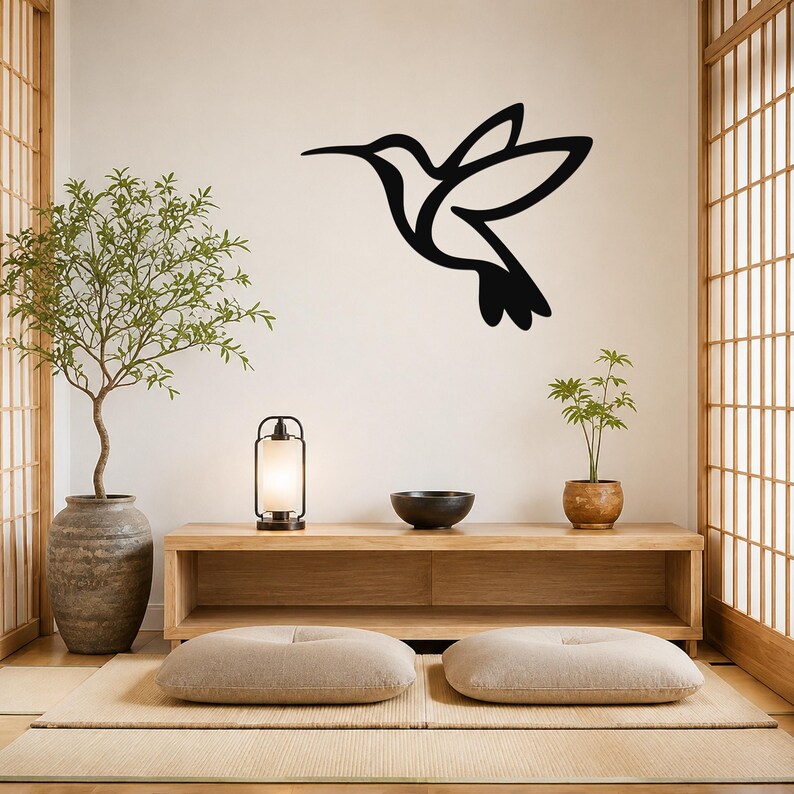Black metal hummingbird wall art with a silhouette cutout design, mounted on a wall above a wooden console in a minimalist room.