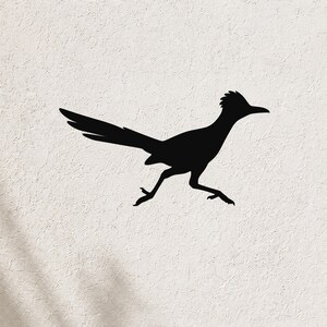 Black metal roadrunner wall art silhouette with outstretched wings and long tail, mounted on a textured white wall.