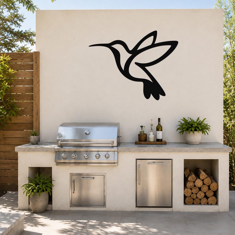 Black metal hummingbird wall art silhouette mounted on an outdoor kitchen wall above a stainless steel grill and counter.