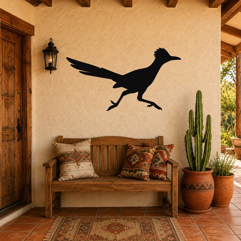 Black metal roadrunner wall art silhouette mounted on a stucco wall above a wooden bench in a southwestern-style patio entry.