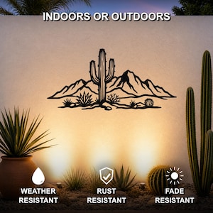 Black metal wall art featuring a desert landscape silhouette with a saguaro cactus and mountains, mounted on an outdoor wall above a gravel garden with potted cacti.