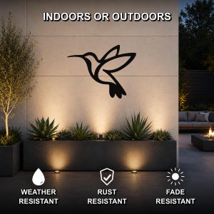 Black metal hummingbird wall art silhouette mounted on an outdoor wall above a planter, with text indicating it is weather, rust, and fade resistant.