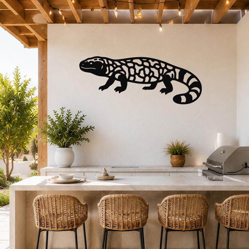 Black metal Gila monster wall art with intricate cutout patterns, mounted on a white outdoor wall above a kitchen counter.
