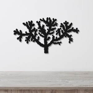Black metal wall art cutout of a cholla cactus with branching arms, mounted on a white wall above a light wood surface.