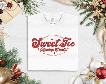 Könnte beinhalten: Ein weißes T-Shirt mit dem roten Text "Sweet Tee Mockup Studio", umgeben von festlichen Weihnachtsdekorationen. Der Text enthält die Sätze "True-to-life POD Mockups" und "Real Mockups Real Success".