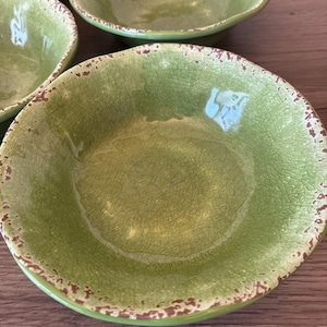 May include: A close-up of several green ceramic bowls with a distressed, crackled finish. The bowls have a slightly irregular shape and a brown rim. The bowls are likely for serving food.