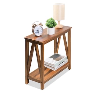 May include: A wooden side table with a lower shelf and angled legs. The table is topped with a small lamp, a potted plant, and a vintage alarm clock. Two books are on the lower shelf. The table is made of a warm-toned wood.