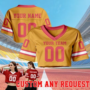 May include: Mustard yellow crop top football jersey with pink accents and the text "YOUR TEAM" and "YOUR NAME". The number "00" is displayed prominently. The text "CUSTOM ANY REQUEST" is at the bottom.