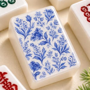 May include: A rectangular mahjong tile with an off-white base featuring a detailed blue floral pattern on its face. The design consists of various stylised flowers and leaves arranged across the surface, surrounded by other game tiles.