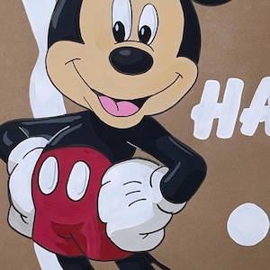 May include: A hand-painted wooden cutout of Mickey Mouse featuring a black head and body, white gloves, red shorts with two white oval buttons, and large yellow shoes. The character stands against a brown background with white accents and text.