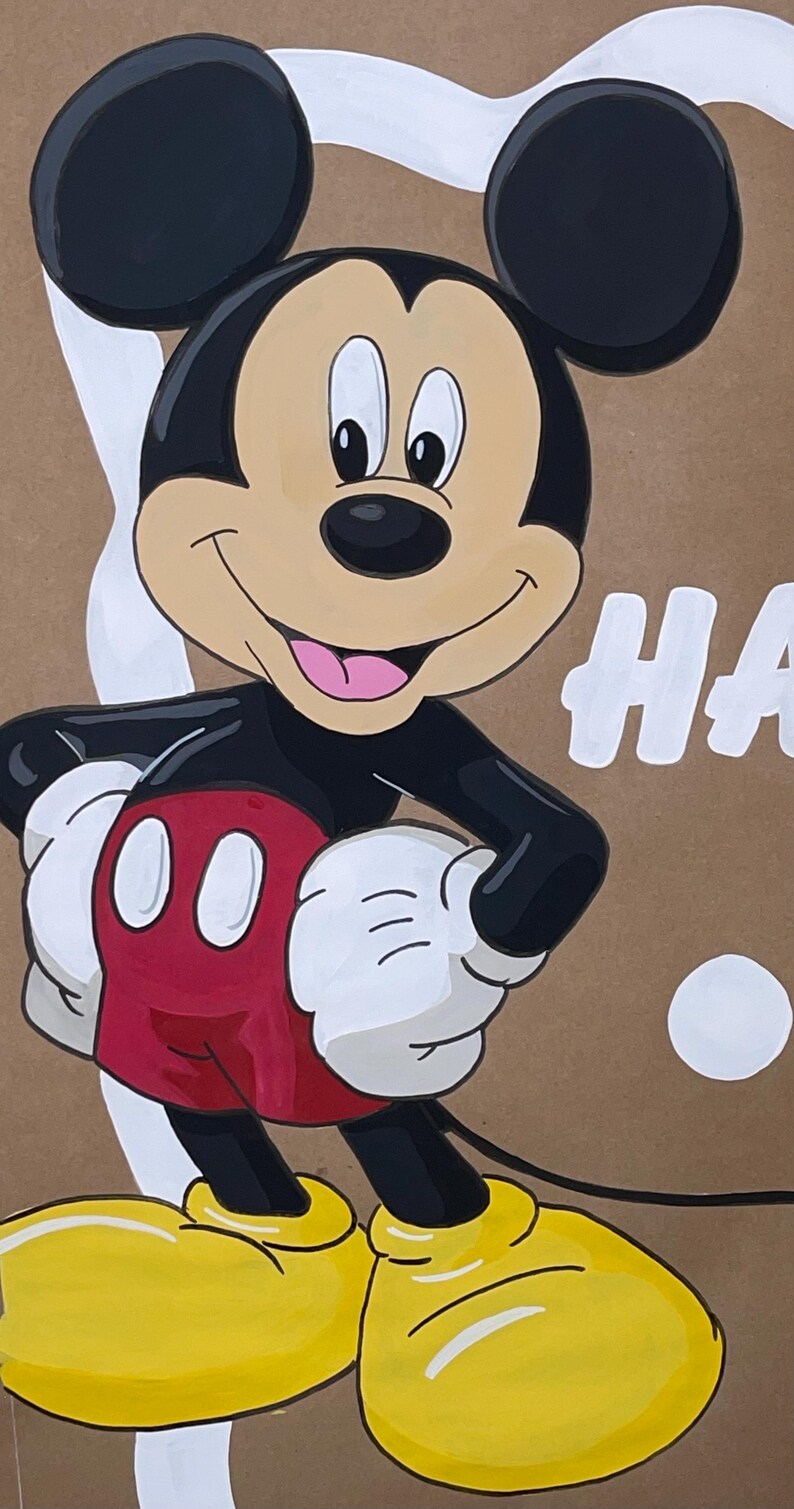May include: A hand-painted wooden cutout of Mickey Mouse featuring a black head and body, white gloves, red shorts with two white oval buttons, and large yellow shoes. The character stands against a brown background with white accents and text.