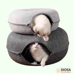 May include: Two gray cat beds stacked on top of each other. Each bed has a zippered opening and a cat inside. The cats are white with gray markings. The beds are made of a felt-like material.