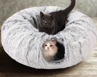 May include: A gray and white plush cat bed with two cats inside. One cat is gray and the other is white and gray. The bed is round and has a soft, fluffy texture, providing a cozy space for pets.