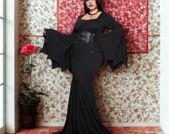 May include: A black, long-sleeved dress with flared sleeves and a mermaid-style skirt. The dress features a square neckline and a wide, cinched waist belt. A decorative headpiece and necklace complete the look. The background has a floral pattern.