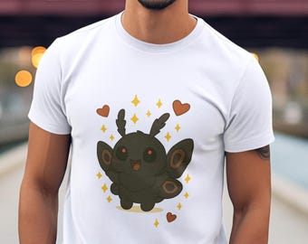 Puede incluir: Camiseta blanca con un diseño de polilla de dibujos animados, corazones y estrellas. La polilla es de color marrón oscuro con orejas y alas grandes. La camiseta la lleva una persona con pantalones color turquesa.