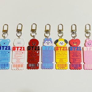 May include: Seven acrylic keychains featuring BT21 characters Koya, RJ, Shooky, Mang, Chimmy, Tata, and Cooky. Each keychain is shaped like a ticket with the character head at the top, the BT21 logo, printed character details, and a barcode at the base.