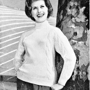 Può includere: Immagine in bianco e nero di una donna che indossa un maglione a collo alto bianco con dettagli a trecce sulle maniche. La donna sorride e sembra appoggiata a un albero. Estetica vintage.