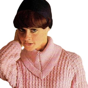 May include: A pink knitted sweater with a textured design and a wide collar. The sweater is worn with a black cap. The image is a close-up, showing the details of the knitwear. The sweater's design is reminiscent of vintage fashion.