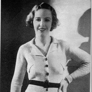 May include: A vintage black and white image of a woman wearing a light-colored cardigan with a black belt. The cardigan has a collared neckline and button closure. The image includes text that reads, "We must admit we're rather proud of this sporty cardigan..."