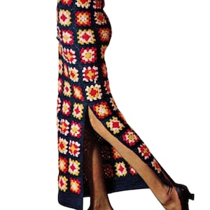 May include: A long, navy blue crochet skirt with a high slit, featuring a repeating pattern of colorful floral squares in red, yellow, and white. The skirt is paired with black shoes.