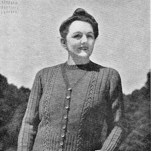 May include: A woman in a dark knitted cardigan and skirt. The cardigan features a button closure and cable knit design. The black and white image includes the text "PATONS & BALDWINS" in the bottom right corner, suggesting a vintage fashion piece.