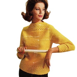 Könnte beinhalten: Ein gelber Vintage-Strickpullover mit strukturiertem Ausschnitt und Bündchen. Der Pullover hat einen U-Boot-Ausschnitt und lange Ärmel. Das Design umfasst horizontale weiße Streifen. Das Model trägt eine schwarze Hose.