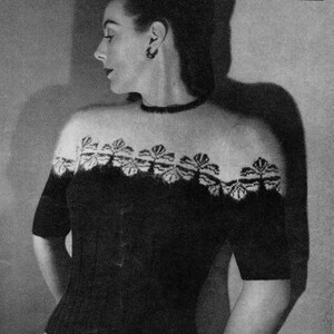 May include: A black and white photograph of a woman wearing a short-sleeved sweater. The sweater has a floral design across the chest and shoulders. The woman is wearing a choker necklace and earrings. The image is a vintage fashion portrait.