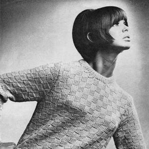 Könnte beinhalten: Schwarz-Weiß-Foto einer Person in einem hellen, strukturierten Pullover. Der Pullover hat ein geometrisches Karomuster. Die Person lehnt sich auf eine Oberfläche, wobei ihr Arm darauf ruht. Der Pullover hat lange Ärmel und einen Rundhalsausschnitt.