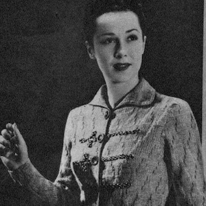 May include: A long, button-down dress with a textured pattern. The dress has a collared neckline and long sleeves. The dress is knee-length and appears to be made of a woven fabric.