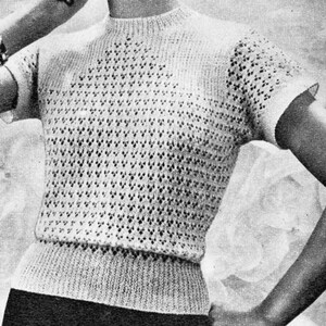 Op de afbeelding: Een off-white gebreide top met korte mouwen en een hoge halslijn. Het kledingstuk heeft een openwerkpatroon over de borst en mouwen, en een geribbelde band in de taille. De stijl is vintage, met een textuurontwerp. De mouwen zijn kort.