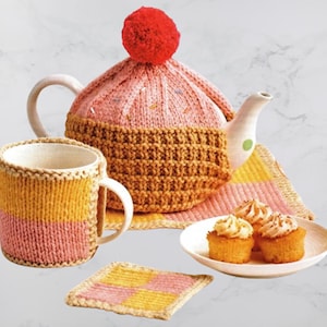 May include: A whimsical tea set featuring a pink and brown knitted teapot cozy with a red pom-pom, a matching mug, a coaster, and a plate of cupcakes. The set has a handmade aesthetic with a playful, dessert-themed design.