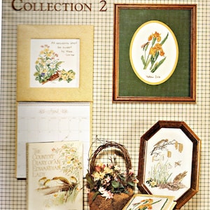 Puede incluir: Una exhibición de arte de punto de cruz y artículos relacionados. Incluye piezas enmarcadas con diseños florales y de aves, un calendario, un libro titulado "The Country Diary of an Edwardian Lady" y una cesta de flores. El texto "The Country Diary Collection 2" es visible.