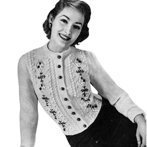 May include: A vintage, cream-colored cardigan sweater with a round neckline and button-up front. The sweater features textured knit patterns and black floral embroidery. The sleeves are long, and the overall style is classic and timeless.