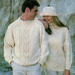 May include: Two cream-coloured cable knit jumpers featuring a central vertical braided pattern and ribbed detailing. One jumper has a crew neckline, while the other features a high turtleneck collar. Both garments are long-sleeved with ribbed cuffs.