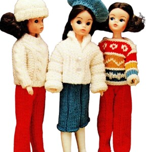 May include: Three vintage dolls in knitted winter clothing. The dolls are wearing white sweaters, red trousers, and hats. One doll has a white knitted hat with a pom-pom, another a blue beret, and the third a red, white, and yellow patterned sweater.