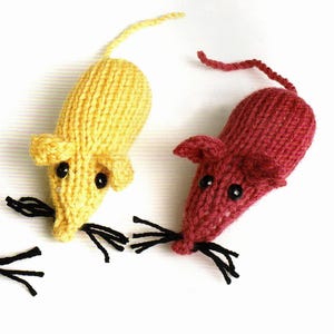 May include: Two small knitted mouse toys, one in bright yellow and one in deep red. Each mouse features a textured yarn body, two small rounded ears, a long thin tail, black bead eyes, and three black yarn whiskers on each side of the snout.