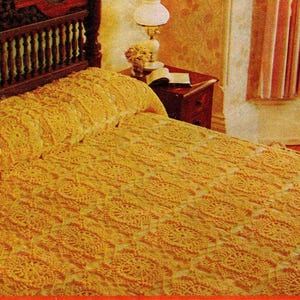 May include: A handmade, golden-yellow crochet bedspread with a repeating floral pattern covers a bed. The bed has a dark wooden headboard. A nightstand with a lamp and a book sits beside the bed. The room has a vintage aesthetic.