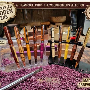 May include: A collection of nine handcrafted wooden pens with varied grain patterns and colors, including brown, yellow, and purple, displayed on two tiered stands. The pens feature metal clips and tips, with text overlays including Handcrafted Wooden Pens.